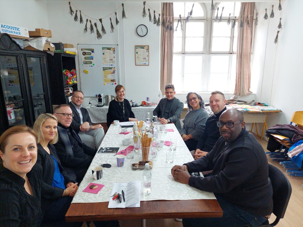 20260123_112650 Na sliki so ljudje iz Amerike, ki so bili gostitelji CDI Univerzuma. Sedijo za veliki dolgo mizo.