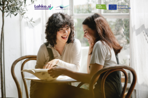 Dve dekleti sedita za okroglo mizo, ki sta nasmejani, saj bereta knjigo. Sta rjavolasi z srednje dolgimi lasmi, oblečeni obe v beli majci.